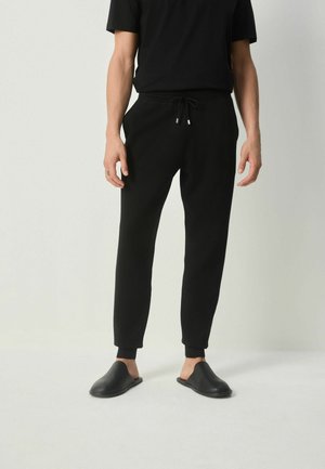 Schwarze Jogginghosen mit einem Kordelzugbund, schmaler Schnitt, mit Bündchen am Knöchel, kombiniert mit einem schwarzen T-Shirt und schwarzen Slippern.