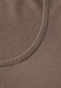 Brown fabric showing a smooth texture with a curved seam. The material is slightly glossy, with even stitches along the edges.