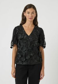 Zwarte blouse met V-hals, versierd met textuurrijk bloemrijk borduurwerk en doorschijnende pofmouwen. Voorzien van een ontspannen pasvorm en lichtgewicht stof.
