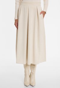 Beige corduroy midi skirt with pleats and side pockets. Features a high waistband and smooth texture. Paired with knee-high beige boots.