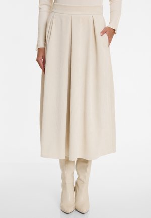 Beige corduroy midi-rok met plooien en zijzakken. Heeft een hoge tailleband en een gladde textuur. Gecombineerd met beige laarzen tot de knie.