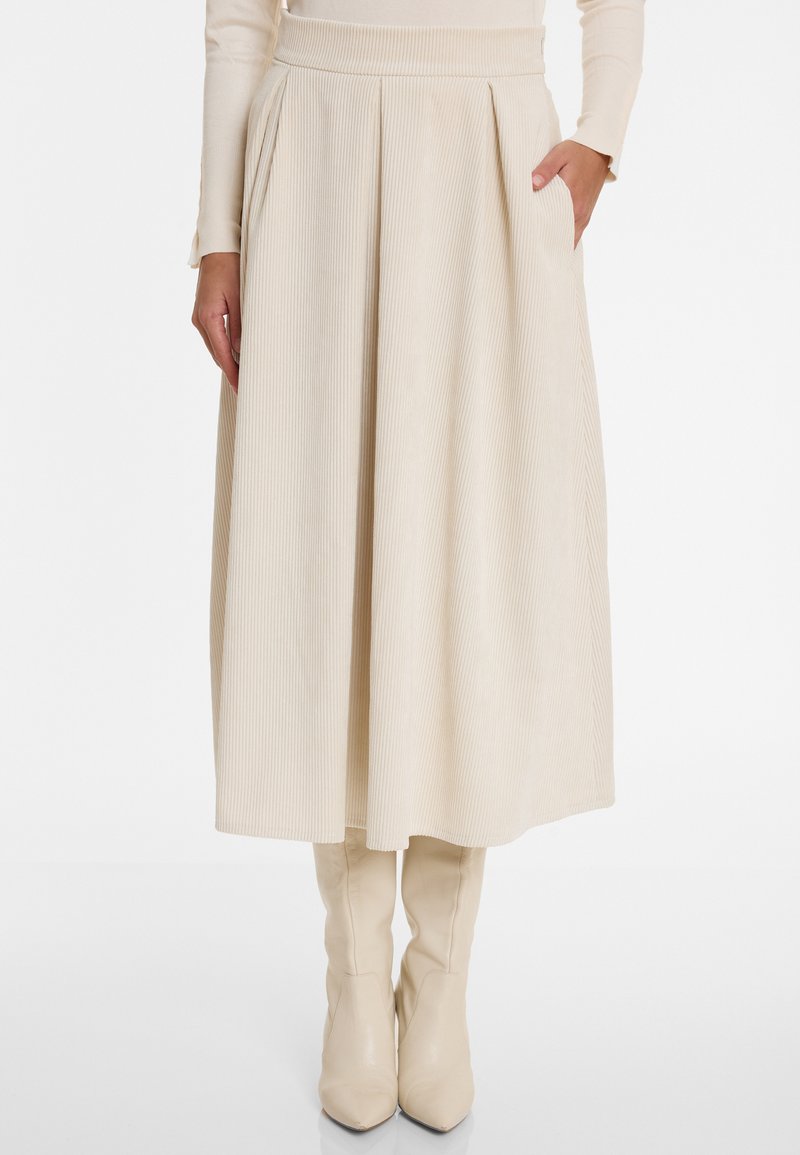 Beige corduroy midi skirt with pleats and side pockets. Features a high waistband and smooth texture. Paired with knee-high beige boots.