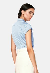 Light blue short-sleeve polo shirt with a pointed collar and a structured back design, paired with a high-waisted cream skirt.