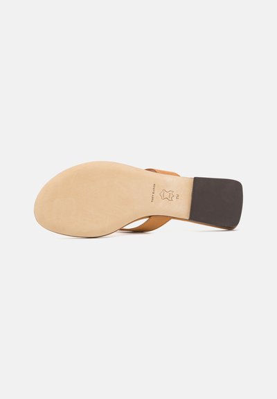 Sandalia de cuero marrón con una suela plana de color claro, que presenta un diseño de tiras cruzadas y un tacón rectangular negro.