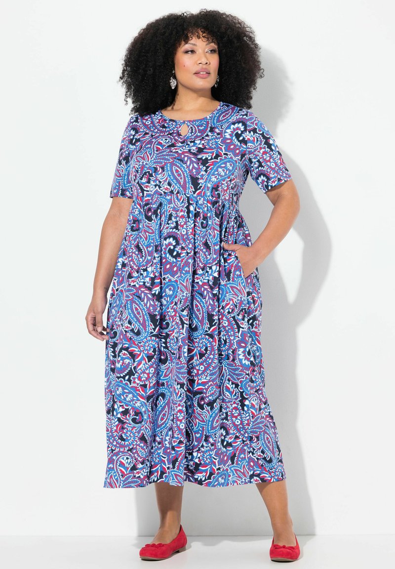 Vestido maxi con un patrón de cachemira, que presenta un escote redondo con un detalle de ojal, mangas cortas y bolsillos laterales. Los colores incluyen azul, rojo y blanco.