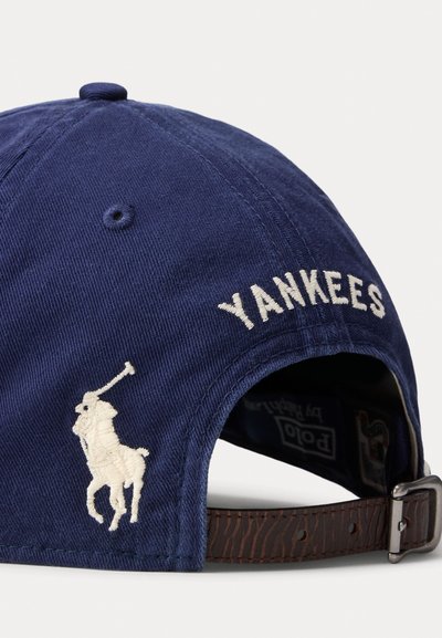 Ναυτικό μπλε καπέλο με κεντημένο το κείμενο «YANKEES» σε λευκό, που διαθέτει λογότυπο παίκτη polo σε κρεμ χρώμα; δερμάτινο λουράκι με μεταλλική ζώνη.