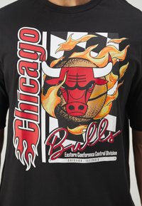 Schwarzes Baumwoll-T-Shirt mit einem grafischen Motiv des Chicago Bulls-Logos, umgeben von Flammen, kräftigen roten und gelben Akzenten sowie weißem Text.