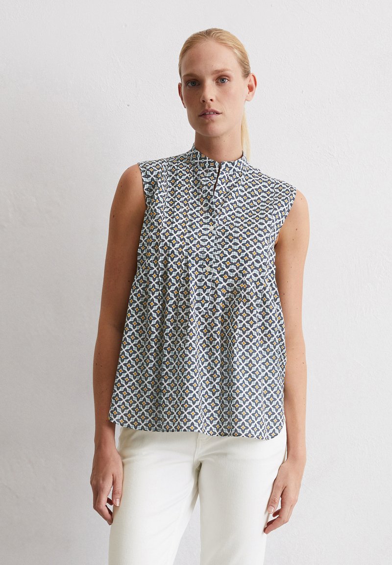 �Ärmellose Bluse in Hellblau mit einem geometrischen Muster in Gelb und Marineblau. Sie hat einen Stehkragen und eine Knopfleiste vorne.