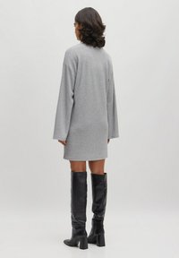 Graues, geripptes Strickkleid mit langen Ärmeln, das bis zur Mitte des Oberschenkels reicht. Kombiniert mit schwarzen, kniehohen Lederstiefeln und einer geraden Silhouette.