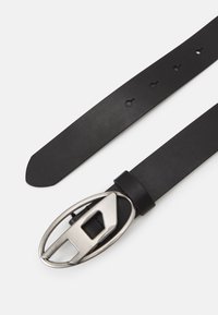 Ceinture en cuir noir avec une boucle ovale en argent au design découpé, texture lisse, et plusieurs trous d'ajustement le long de la sangle.