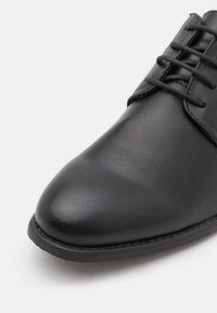 Scarpe eleganti in pelle nera con texture liscia, punta rotonda e design con lacci. Presentano una suola cucita per una maggiore durata.