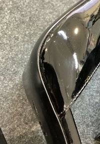 Gros plan d’un talon de chaussure en cuir verni noir brillant posé sur un sol recouvert de moquette grise.
