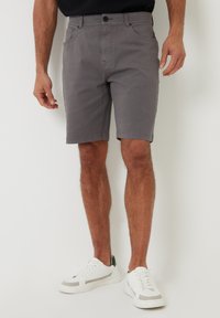 Grå bomuldsshorts med flad front, fem lommer og knaplukning. Båret med hvide sneakers. Slim fit med en glat tekstur.