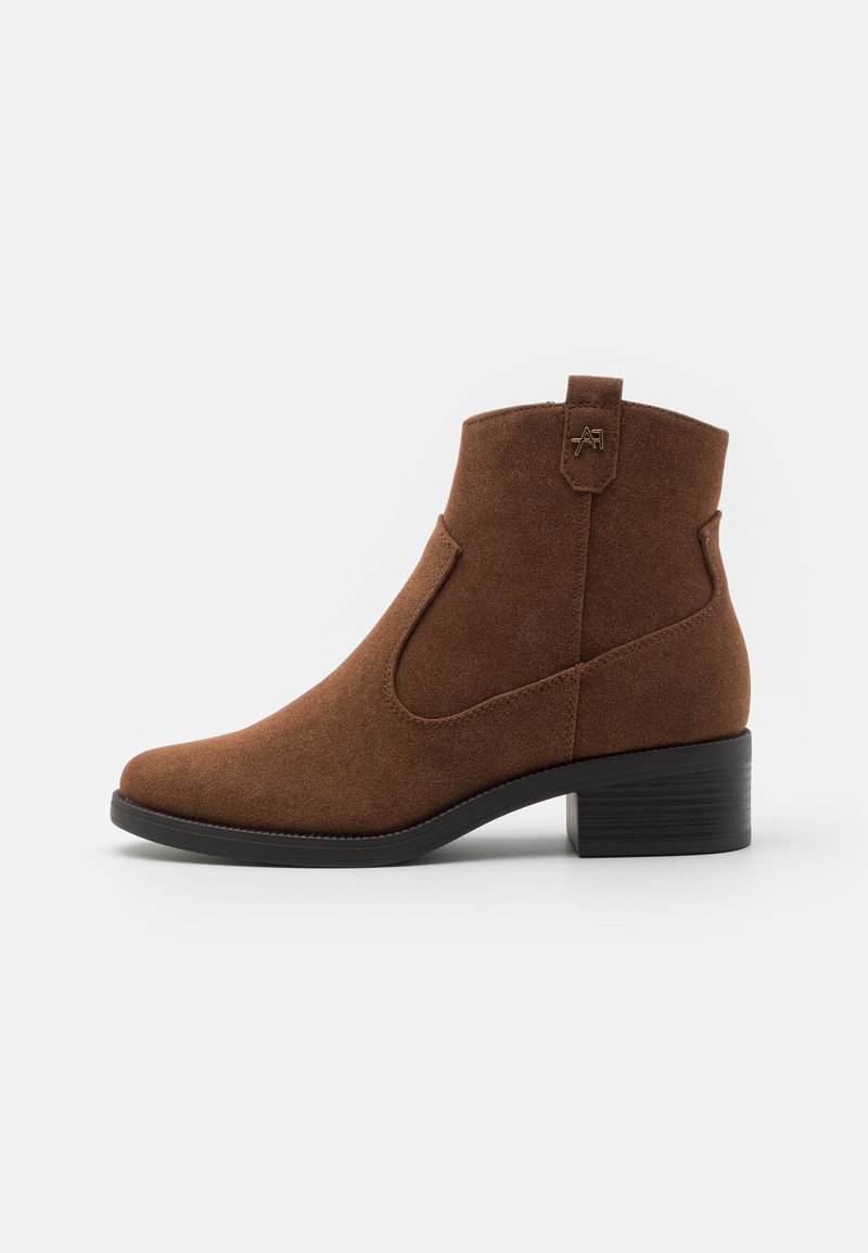 Bottine en daim marron avec un petit talon empilé, languette de tirage et détails de couture subtils sur fond blanc.