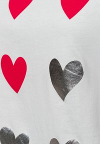 White fabric with red and metallic silver heart patterns, featuring distinct shapes and smooth textures.