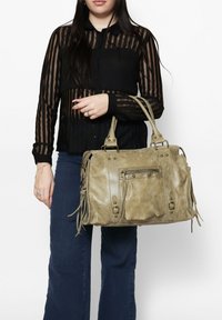Borsa a tracolla in finta pelle beige con due manici superiori, dotata di tasca frontale con zip, borchie in metallo e dettagli in frange.
