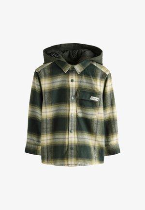 Lapsen vihreä ja beige ruutuintarjoustakki, jossa on nepparit ja rintatasku, jossa lukee "LEIKI ILMAN RAJOJA."