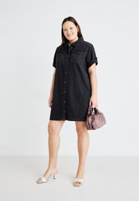 Black denim shirt dress with short sleeves, button-down front, two chest pockets, paired with a mauve handbag and white open-toe heels.