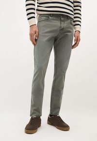 Graue Denim-Jeans mit slim Fit, die ein klassisches Fünf-Taschen-Design und dezente Stickdetails aufweisen. Getragen mit braunen Sneakers.
