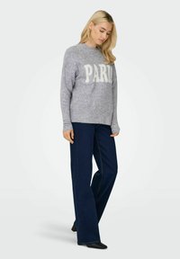 Un pull en tricot gris avec le mot "PARIS" en blanc, associé à un jean large bleu foncé et des chaussures noires à bout pointu.