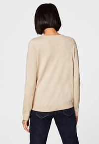 Beige knitted sweater with long sleeves, round neckline, and ribbed hem, paired with dark blue jeans. Simple and textured design.