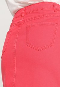 Jupe en denim rose, taille haute, avec poches arrière et une texture lisse. Détails de couture visibles le long des coutures.