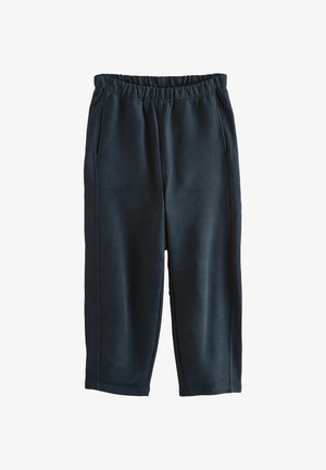 Čierne tepláky z mäkkej tkaniny s elastickým pásom, dvoma bočnými vreckami a viditeľným švom na nohaviciach.