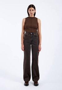 Top marrón sin mangas con textura acanalada y vaqueros acampanados de mezclilla oscura de talle alto, con un ajuste cómodo y detalles mínimos. Color sólido en toda la prenda.