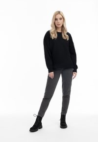Felpa nera con vestibilità ampia, scollo rotondo e maniche lunghe. Abbinata a pantaloni grigi a sigaretta e stivaletti neri.