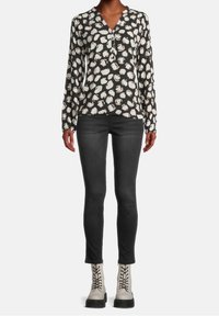 Blusa nera a maniche lunghe con motivi astratti bianchi, abbinata a jeans neri skinny e stivaletti grigi con lacci.
