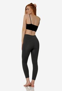 Top corto nero e leggings grigio scuro, entrambi attillati. I leggings hanno una texture liscia e un design a vita alta, senza cuciture visibili.