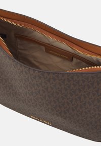 Brun læderpung med tan indvendig, quiltet foring, guld lynlås og signatur Michael Kors-logo på en glat, struktureret overflade.