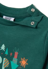 Groene kinderhemd met drukknoopjes op de schouder, voorzien van een feestelijk ontwerp met bomen, ingepakte cadeaus en een oranje sneeuwvlok.