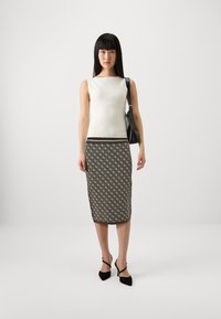 Débardeur blanc à côtes associé à une jupe longueur genou avec un motif géométrique marron, des talons noirs et un sac à main noir.