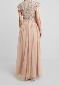 Maxikjol med en figursydd, paljettbeströdd livdel och korta volangärmar. Kjolen är gjord av flödande, lätt tulle i en mjuk nude-färg.