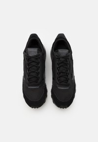 Svarta sportskor i mesh och mocka, med platta snörningar, vadderad tunga och texturerad gummisula. Diskret branding synlig.