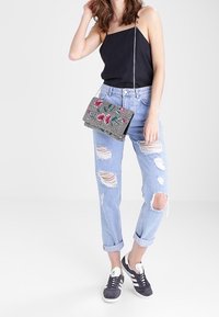 Top negro de tirantes, jeans rasgados azul claro, zapatillas grises. Bolso cruzado gris texturizado con bordado floral. Atuendo casual con un ajuste relajado.