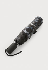 Parapluie noir avec un motif géométrique dans des nuances de bleu, à poignée noire mate et une sangle pour la fermeture. Design compact.