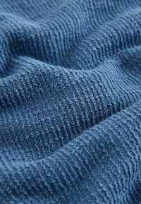 Tissu bleu texturé avec de petites boucles et crêtes surélevées, montré en gros plan, mettant en valeur sa surface douce et tactile.