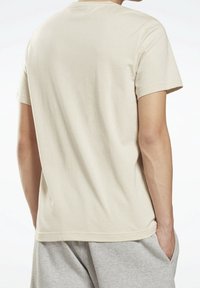 Beige bomull T-shirt med korta ärmar, enfärgad design, rundad halsringning, avslappnad passform, kombinerad med grå shorts, som visar en mjuk textur.