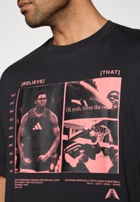 Must lühikeste varrukatega t-särk, millel on roosad graafilised pildid ja tekst. Disain sisaldab korvpalli teemat ja brändi detaile.