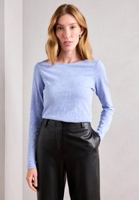 Svijetloplavi dugo rukav top s okruglim izrezom, uparen s crnim kožnim hlačama visokog struka. Glatka tekstura, minimalni uzorak, moderni stil.