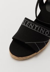 Sandale espadrile negre, realizate din țesătură cu un superior textil. Dispune de o talpă țesută din iută și cusături gri contrastante, inclusiv un logo.