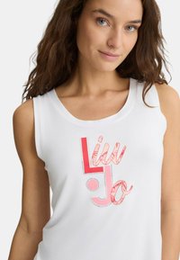 Top bianco senza maniche con un design grafico colorato e testo. Il tessuto appare liscio, con una vestibilità comoda e un collo rotondo.