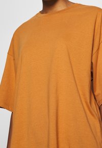 Oranžové tričko s krátkým rukávem z měkké bavlny s volnějším střihem. Má klasický kulatý výstřih a minimální švy.