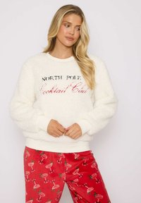 Biały polar z napisem "NORTH POLE Cocktail Club" w czerni i czerwieni. Para czerwonych spodni z wzorem koktajli i zieleni.