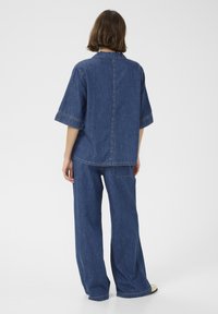 Denim obleka, sestavljena iz ohlapne srajce s kratkimi rokavi in ujemajočih se širokih hlač, v srednje modri barvi, z vidnimi šivi.