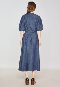 Abito in denim con vita stretta, maniche a palloncino e gonna lunga. Il tessuto presenta un design leggero e testurizzato di colore blu scuro.