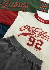 Två t-shirts och mörkgrå shorts liggande platt. T-shirts har kontrasterande färger och tryckta grafik som visar "New York 92" och "Detroit 95."