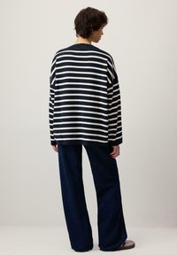 Czarny i biały pasiasty, oversize'owy sweter o luźnym kroju, w połączeniu z ciemnoniebieskimi spodniami o szerokich nogawkach. Miękka tekstura, długie rękawy, prosty design.